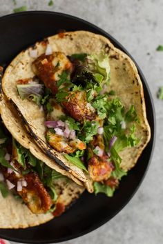 two tacos with meat, lettuce and onions on a black plate next to a pink napkin