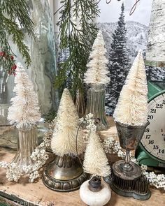 white christmas trees in silver vases on top of a wooden table next to a clock