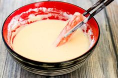 a red bowl filled with cream and two black chopsticks sticking out of it