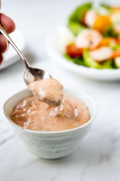 a person holding a spoon full of sauce over a bowl filled with salad and shrimp