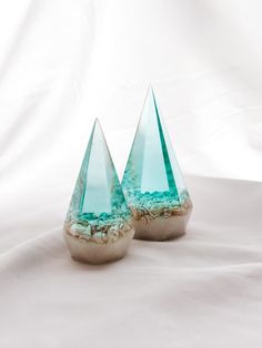 two blue glass vases sitting on top of a white cloth covered table next to each other