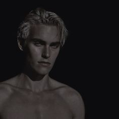 a man with blonde hair and no shirt is looking at the camera while standing in front of a black background