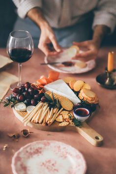 a table topped with cheeses and crackers next to a glass of red wine