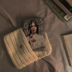 there is a book on the bed next to it and a knitted scarf laying beside it