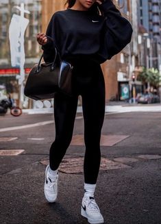 a woman in black is walking down the street with her hand on her hip and wearing white sneakers