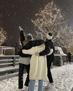 two people hugging each other in the snow at night with fireworks and trees behind them