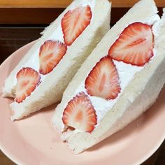 two slices of cake with strawberries on it sitting on a pink plate next to a wooden table