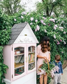 a woman standing next to a child in front of a pink book case with flowers