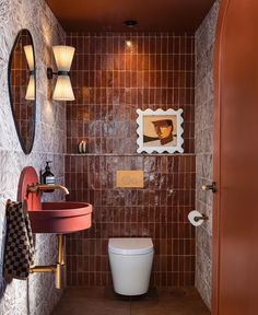 a bathroom with a toilet, sink and mirror in it's corner area next to a tiled wall