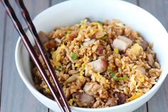 a white bowl filled with rice and meat next to chopsticks on a wooden table