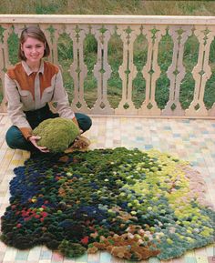 a woman sitting on the ground with a rug made out of balls and yarns