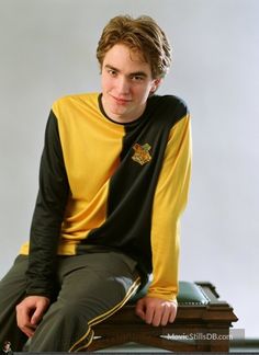 a young man sitting on top of a wooden table wearing a yellow and black shirt