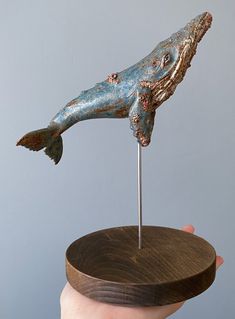 a hand holding a piece of art that looks like a fish on top of a wooden stand