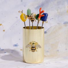 a gold cup with some colorful pins in it and a bee on the side,