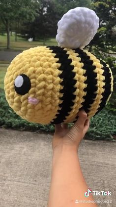 a hand holding up a stuffed bee with a cotton ball on it's head