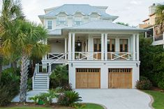 a large white house with two garages on the front and second story, surrounded by palm trees