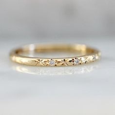 a yellow gold wedding band with three diamonds on the top and bottom, sitting on a white surface