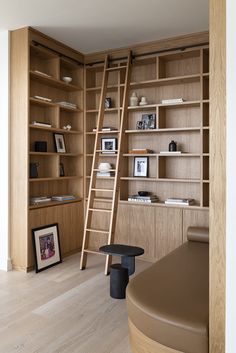 a room with wooden shelves filled with books and pictures next to a ladder that is leaning up against the wall