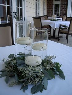 candles are placed in glass vases with greenery on a table outside the house