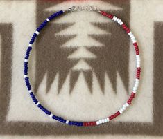 a red, white and blue beaded bracelet with palm trees in the background on a rug