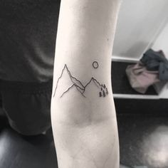 a person with a tattoo on their arm that has mountains and trees in the background