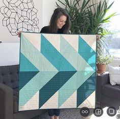 a woman holding up a large blue and white quilt in her living room with a potted plant