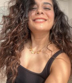 a woman with curly hair smiling and wearing a black tank top