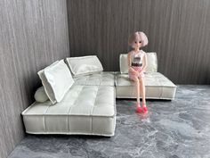 a doll sitting on top of a white couch next to a gray wall and floor