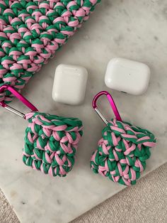 two apple airpodss sitting on top of a marble table next to a pink and green crochet bag