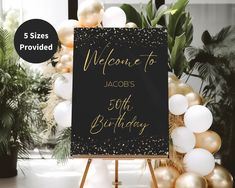 a black and gold welcome sign sitting on top of a easel next to balloons