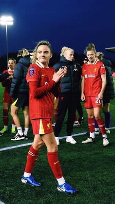 a soccer player is walking on the field with her hands together and other players are in the background