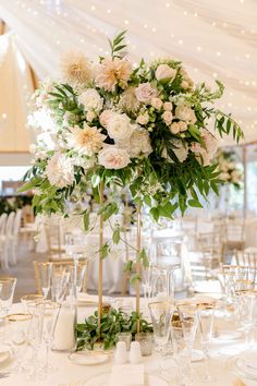 a vase filled with white flowers and greenery on top of a dining room table