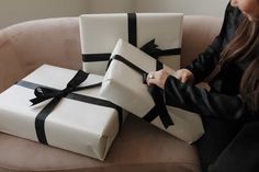 a woman sitting on a couch with two wrapped presents in front of her, one white and the other black