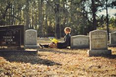 a woman sitting on the ground in front of some headstones and yellow flowers