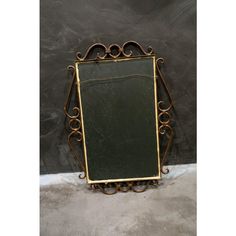 an old fashioned mirror is sitting on the floor in front of a black wall with a gold frame