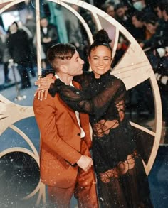 two people standing next to each other in front of a circular object with snow falling on it