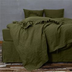 a bed with green sheets and pillows on top of wooden floor next to gray wall