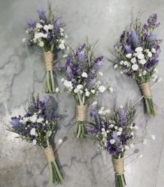 four bouquets of lavender and white flowers on a marble surface with twine tied together