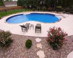 a backyard with a swimming pool and patio furniture set up around the perimeter, surrounded by flowers