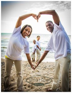 two people making a heart shape with their hands on the beach while others stand in the background