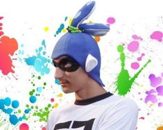 a man wearing a blue bunny ears hat and sunglasses with paint splatters in the background