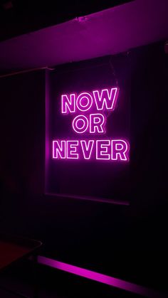 a neon sign that says now or never on the side of a wall in a dark room