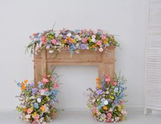 an arrangement of flowers is placed in front of a wooden fire place with white walls