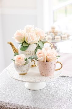 two tea cups with roses in them sitting on a cake stand