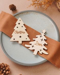 two wooden christmas trees on a plate with brown ribbon and pine cones in the background