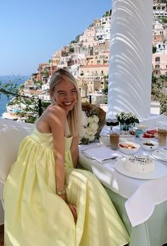 a woman in a yellow dress sitting at a table with a cake and flowers on it