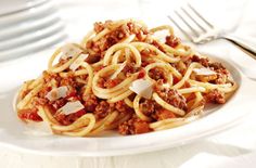 a white plate topped with spaghetti covered in meat and sauce next to silverware on a table