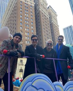 the men are posing for a photo in front of some balloons and buildings on a city street