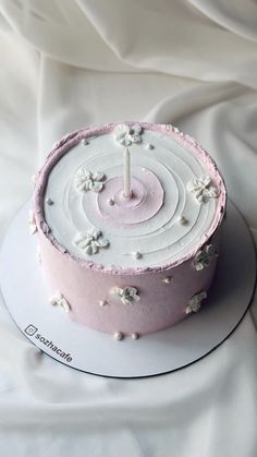 a pink and white cake with a candle on it sitting on a tablecloth covered surface