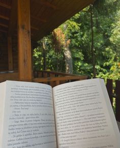 an open book sitting on top of a wooden table next to a forest filled with trees